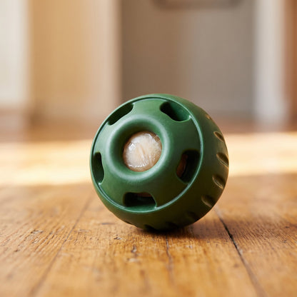 Close-up of the green treat ball on a wooden floor with a frozen treat visible in the opening